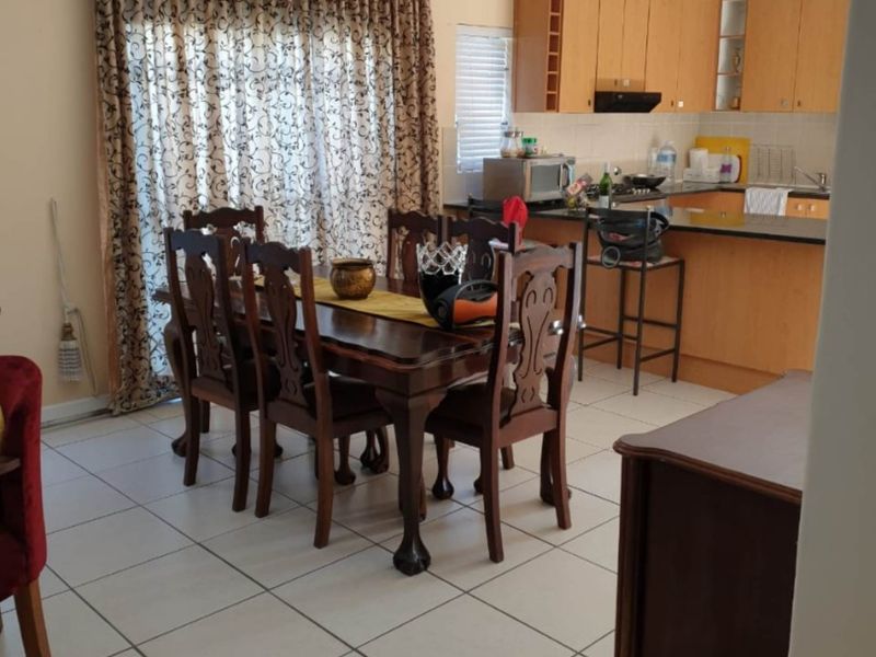 Open-plan dining and kitchen area featuring tiled flooring, wooden cabinetry, and a breakfast bar, with direct access to the outdoor space via sliding doors.