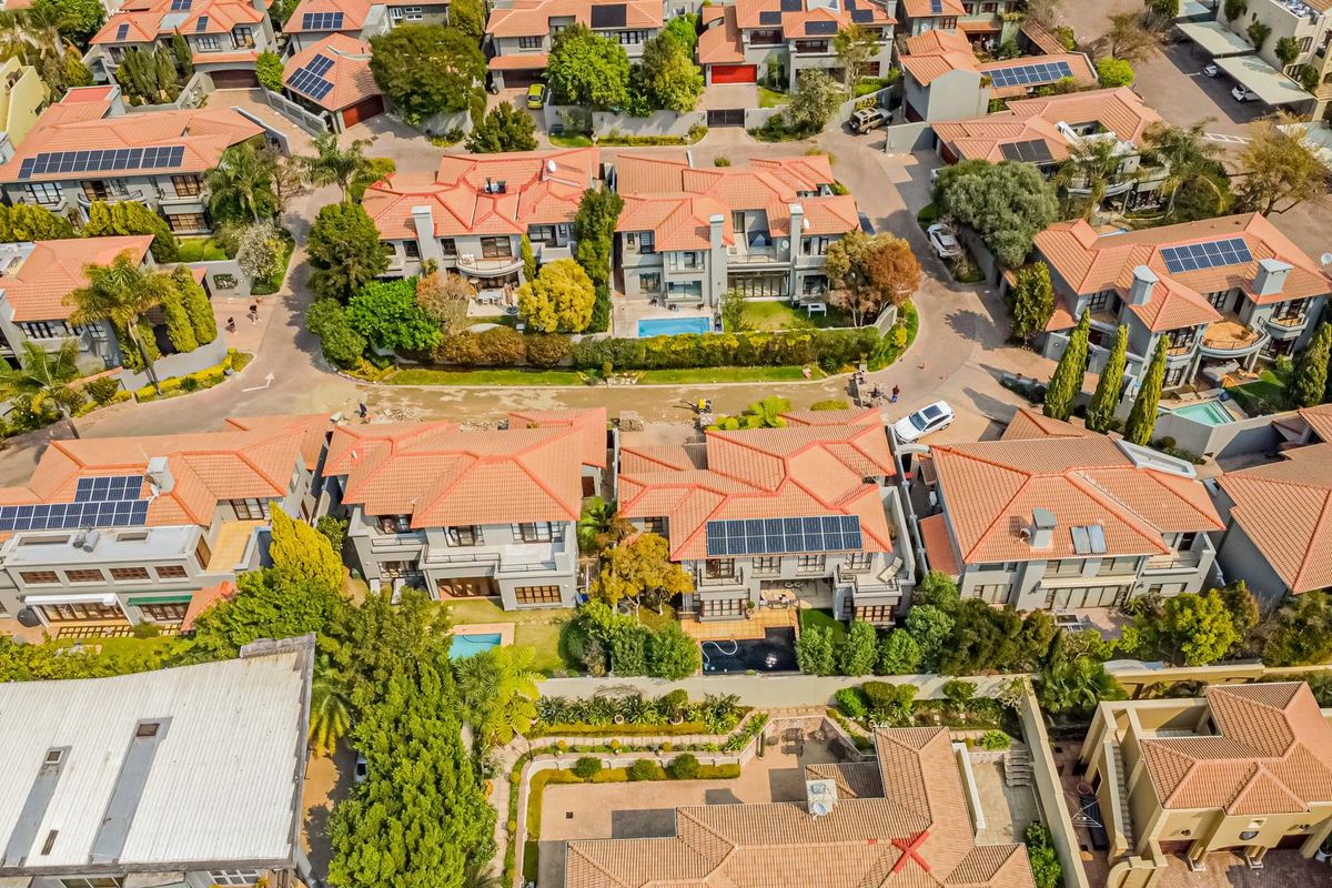 Aerial view of a residential estate featuring multiple detached houses with terracotta tiled roofs, solar panels, and landscaped gardens.