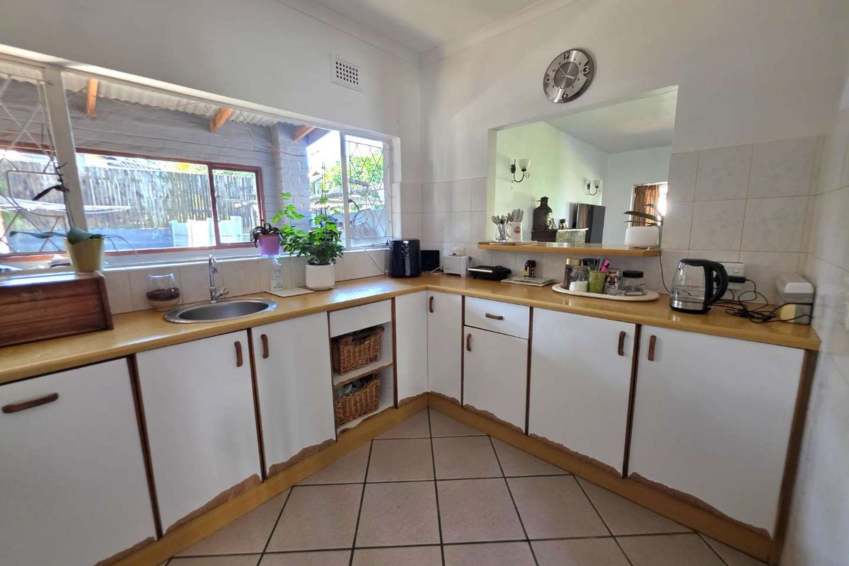 A functional kitchen featuring white cabinetry, laminate countertops, tiled flooring, and a convenient serving window looking into the adjacent living area.