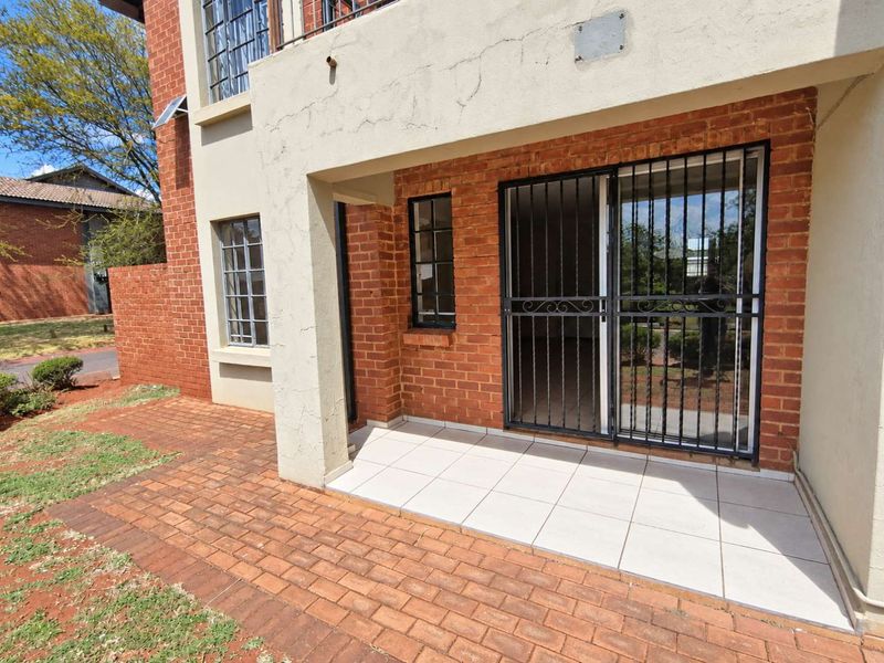A ground-level patio area featuring tiled flooring, brick exterior walls, and a secure sliding door entrance with security bars.