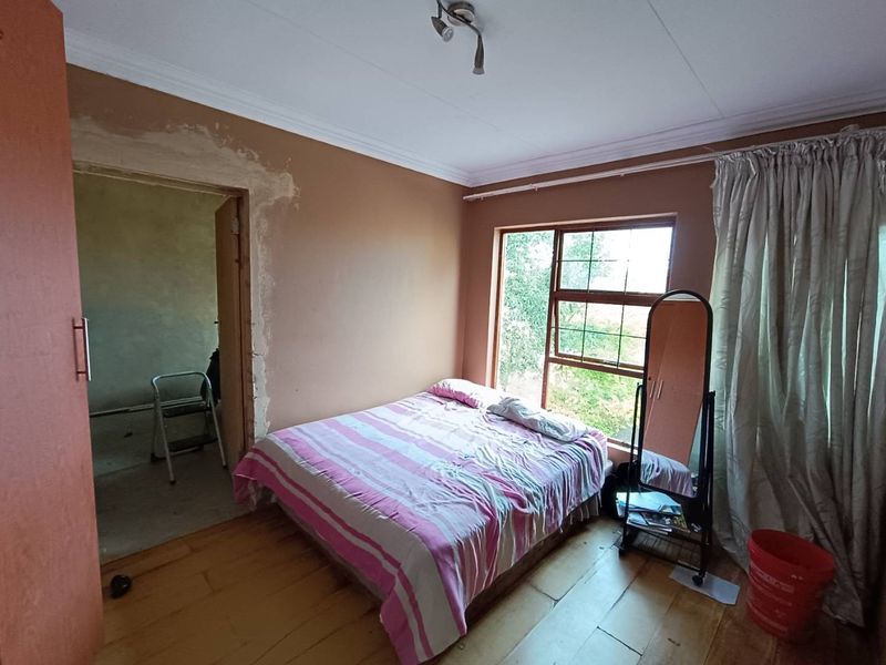A bedroom featuring wooden flooring and natural light, currently requiring cosmetic attention to the wall plaster around the doorway.
