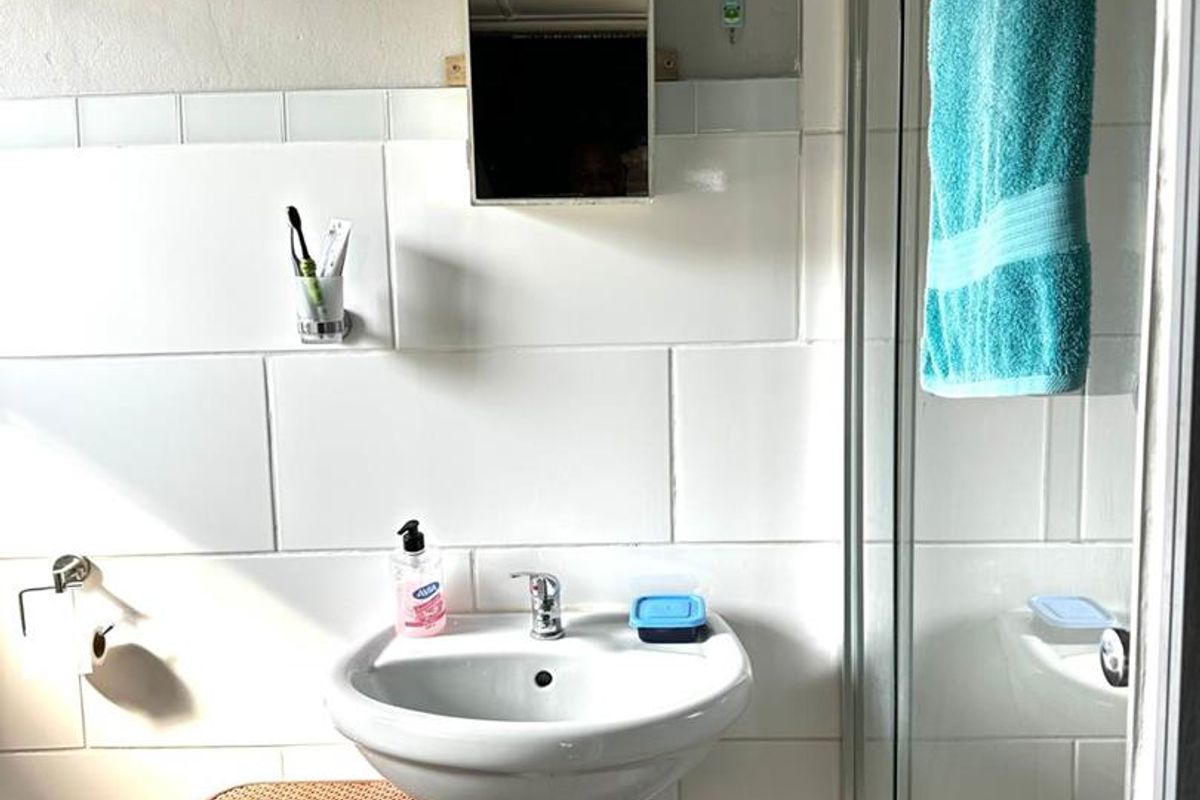 A functional bathroom featuring a pedestal basin, wall-mounted medicine cabinet, and a glass-enclosed shower stall with white wall tiling.