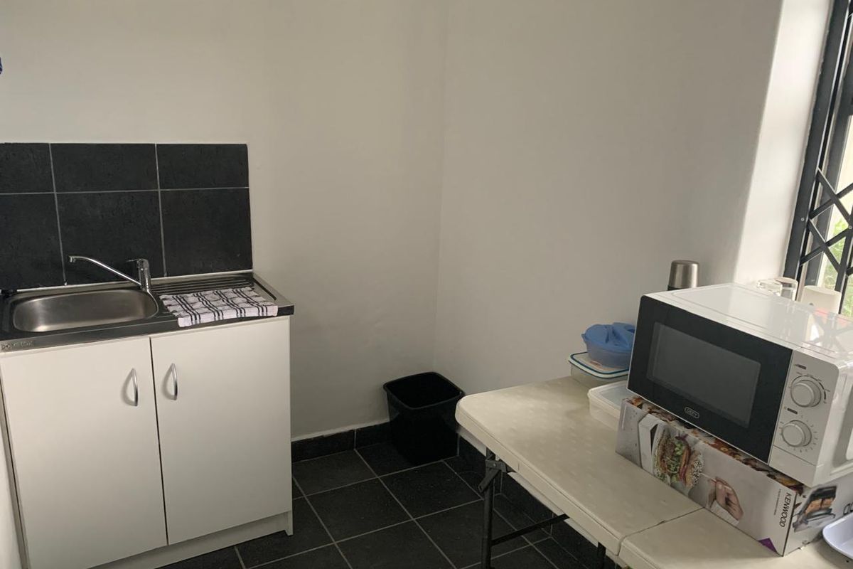 A compact kitchenette area featuring a single sink unit with dark tiled splashback and matching floor tiles.