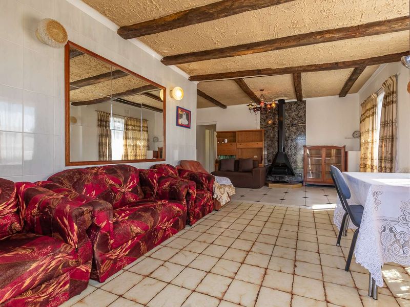 Open-plan living and dining area featuring exposed timber ceiling beams, a central freestanding fireplace, and tiled flooring throughout.