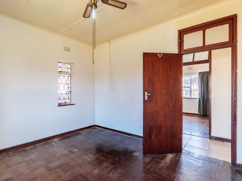An empty bedroom featuring original parquet flooring, a ceiling fan, and a timber door, offering a blank canvas for renovation.