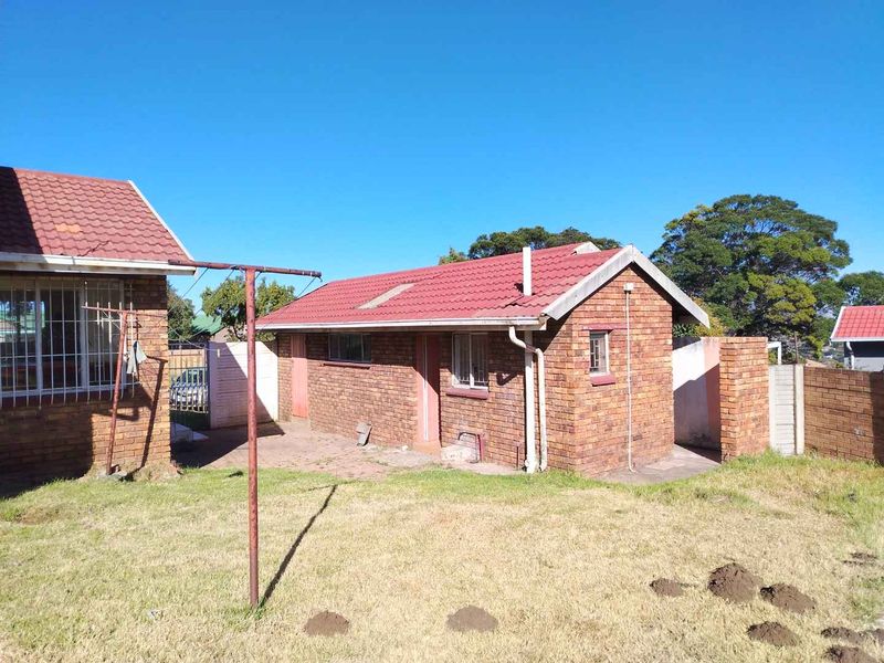 Rear view of the property featuring a brick exterior, tiled roof, and a small backyard area with boundary walls.