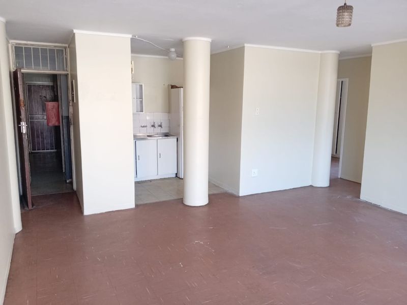 An empty open-plan living area featuring structural columns, a basic kitchenette with sink, and vinyl flooring, offering a blank canvas for renovation.