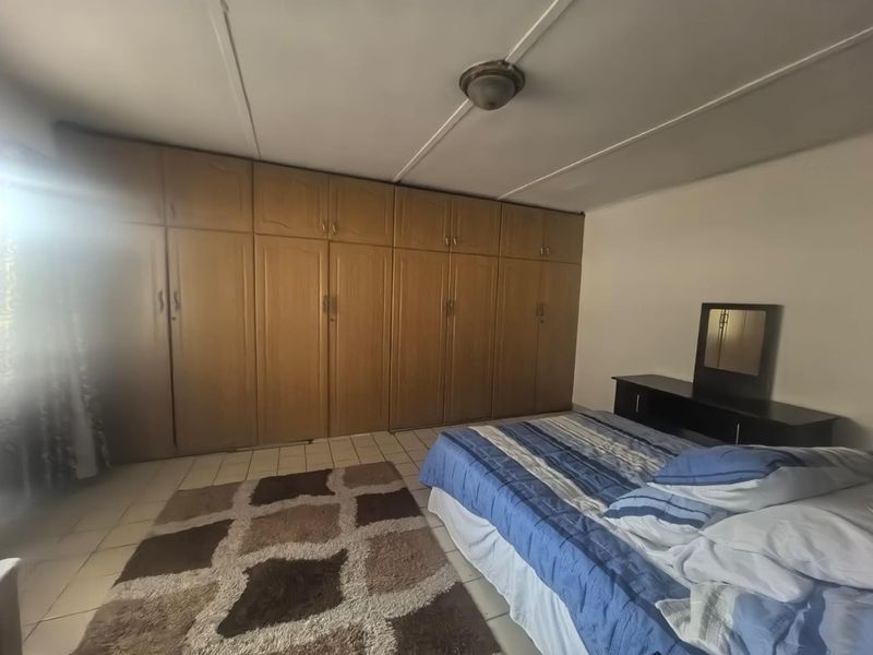 A bedroom featuring extensive wall-to-wall built-in wooden cupboards, tiled flooring, and a central ceiling light fixture.