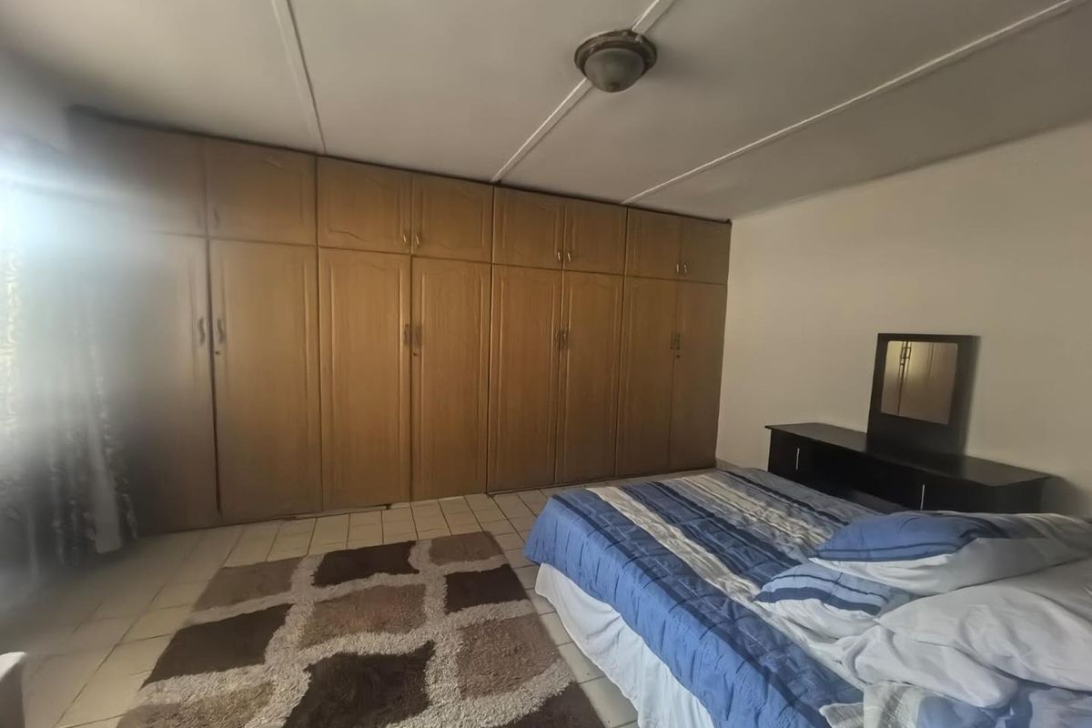 A bedroom featuring extensive wall-to-wall built-in wooden cupboards, tiled flooring, and a central ceiling light fixture.