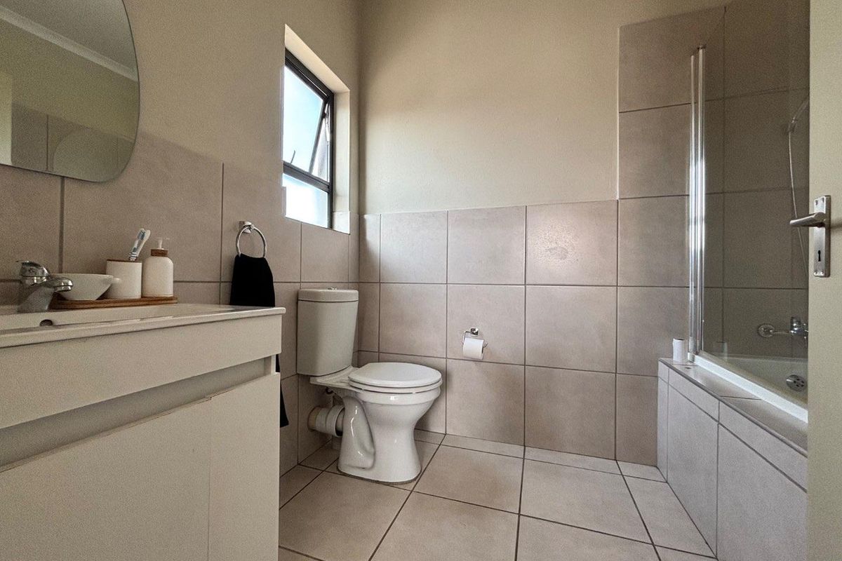 A clean and functional bathroom featuring neutral wall and floor tiling, a built-in vanity, a toilet, and a shower-over-bath combination.