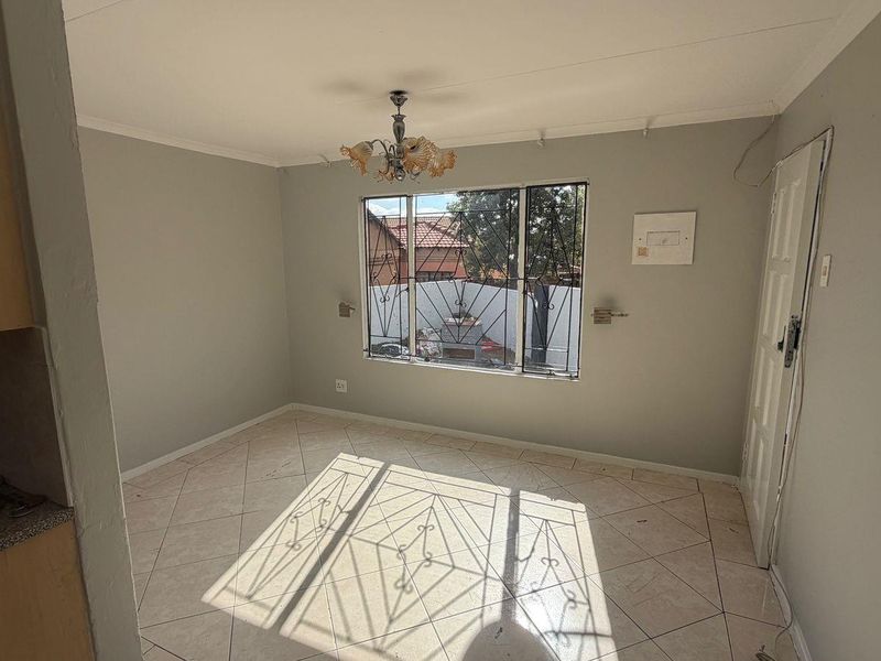 An empty living area featuring tiled flooring, a window with security bars, and a ceiling light fixture, ready for personalization.