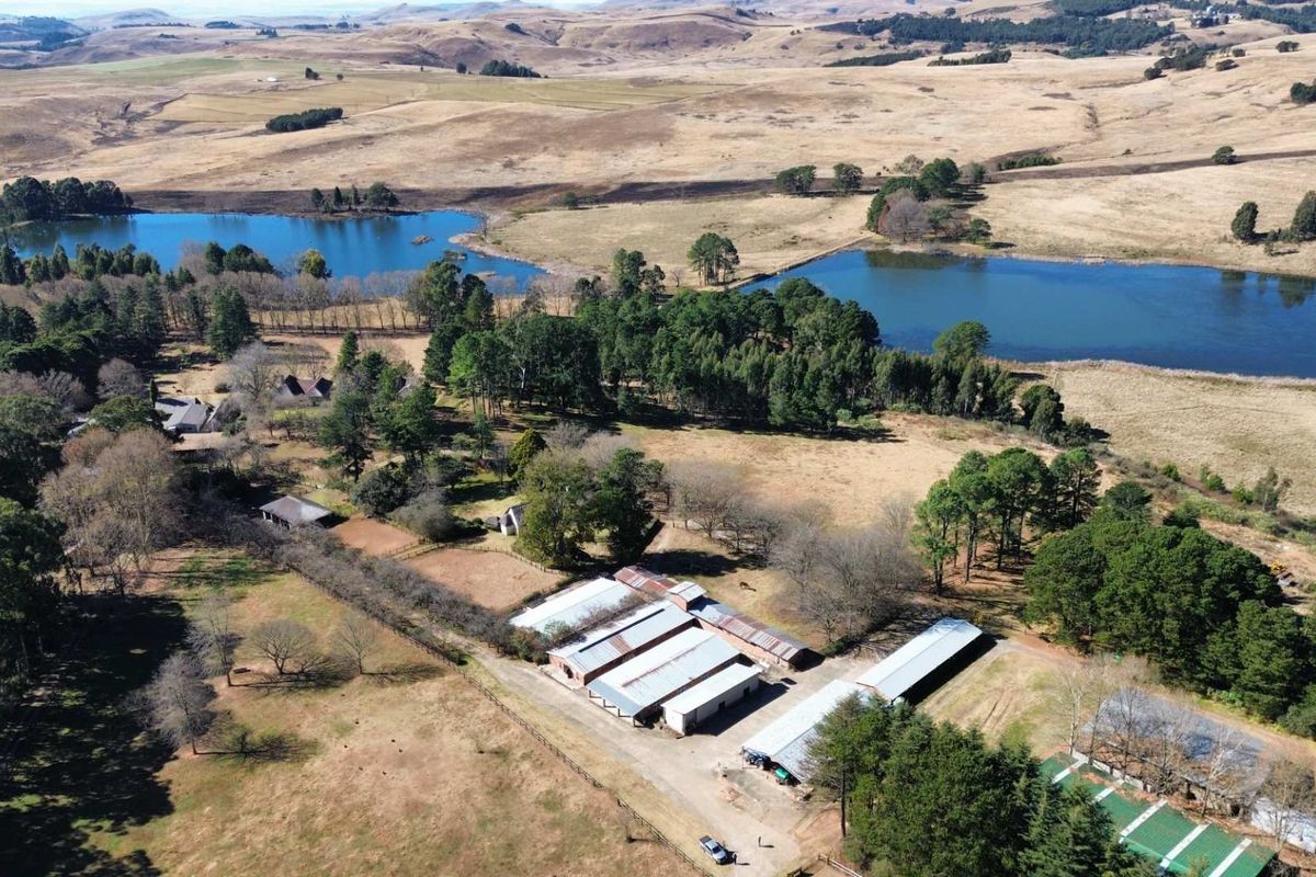 Aerial view of a large farm property featuring multiple outbuildings, stables, and expansive surrounding landscape with two dams.