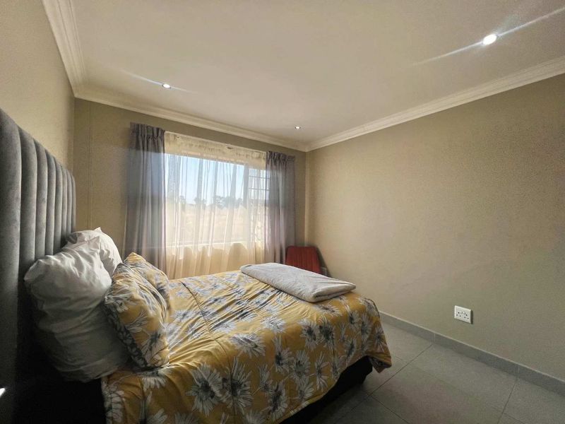 A well-maintained bedroom featuring neutral wall tones, tiled flooring, recessed downlighting, and decorative cornicing.