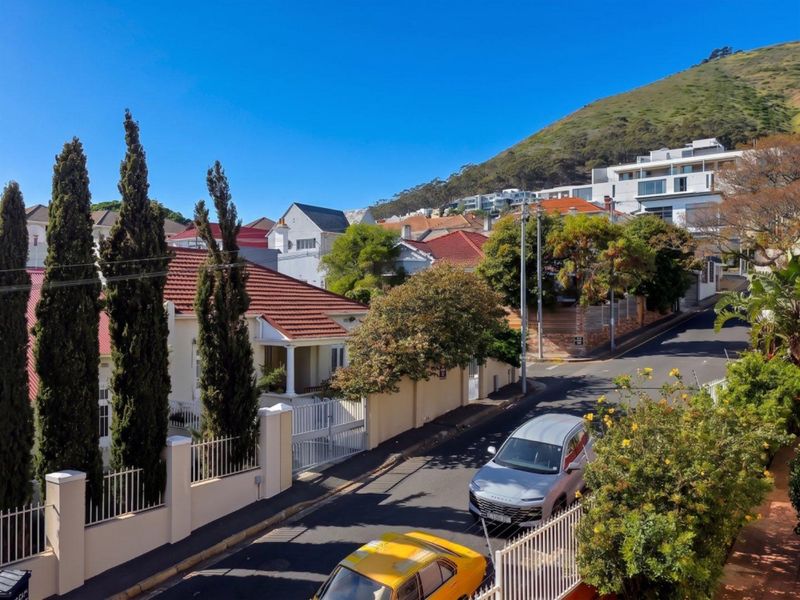 An elevated street view showing the surrounding residential neighbourhood, featuring established boundary walls, tiled roof architecture, and mature trees under a clear sky.