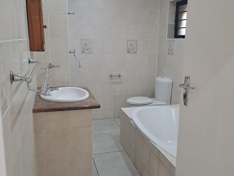 A functional bathroom featuring a built-in bathtub, vanity basin with granite countertop, toilet, and neutral wall and floor tiling.