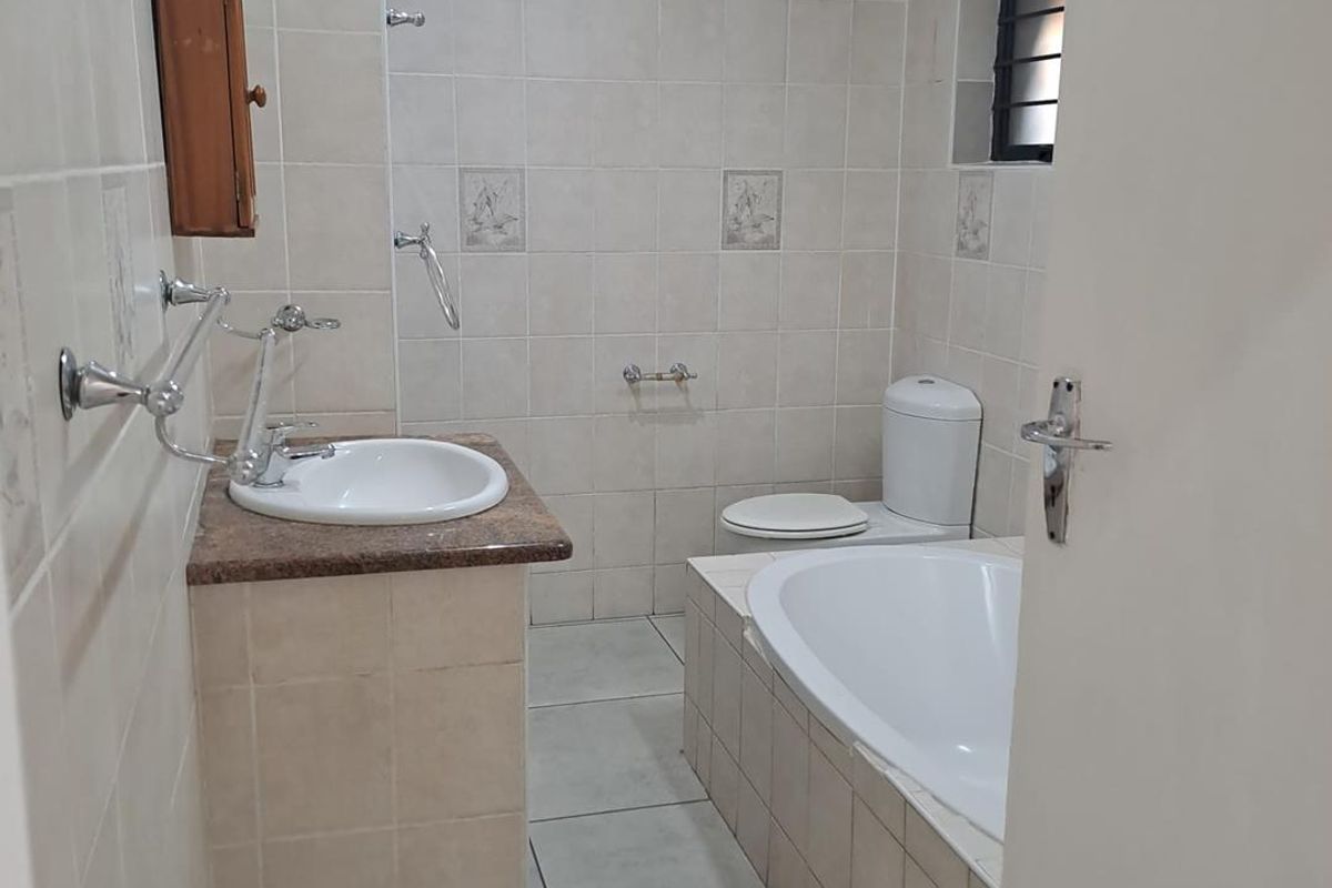 A functional bathroom featuring a built-in bathtub, vanity basin with granite countertop, toilet, and neutral wall and floor tiling.