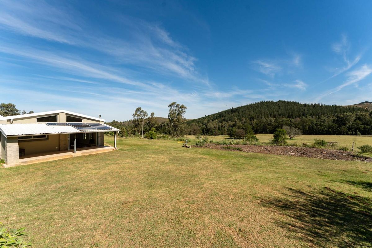 A wide-angle view of the farm property featuring a rear patio, solar panels, and expansive green fields with a scenic mountain backdrop.