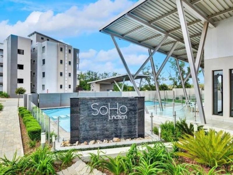 A well-maintained communal pool area at SoHo Junction featuring a modern water feature, glass balustrades, and a covered patio structure.