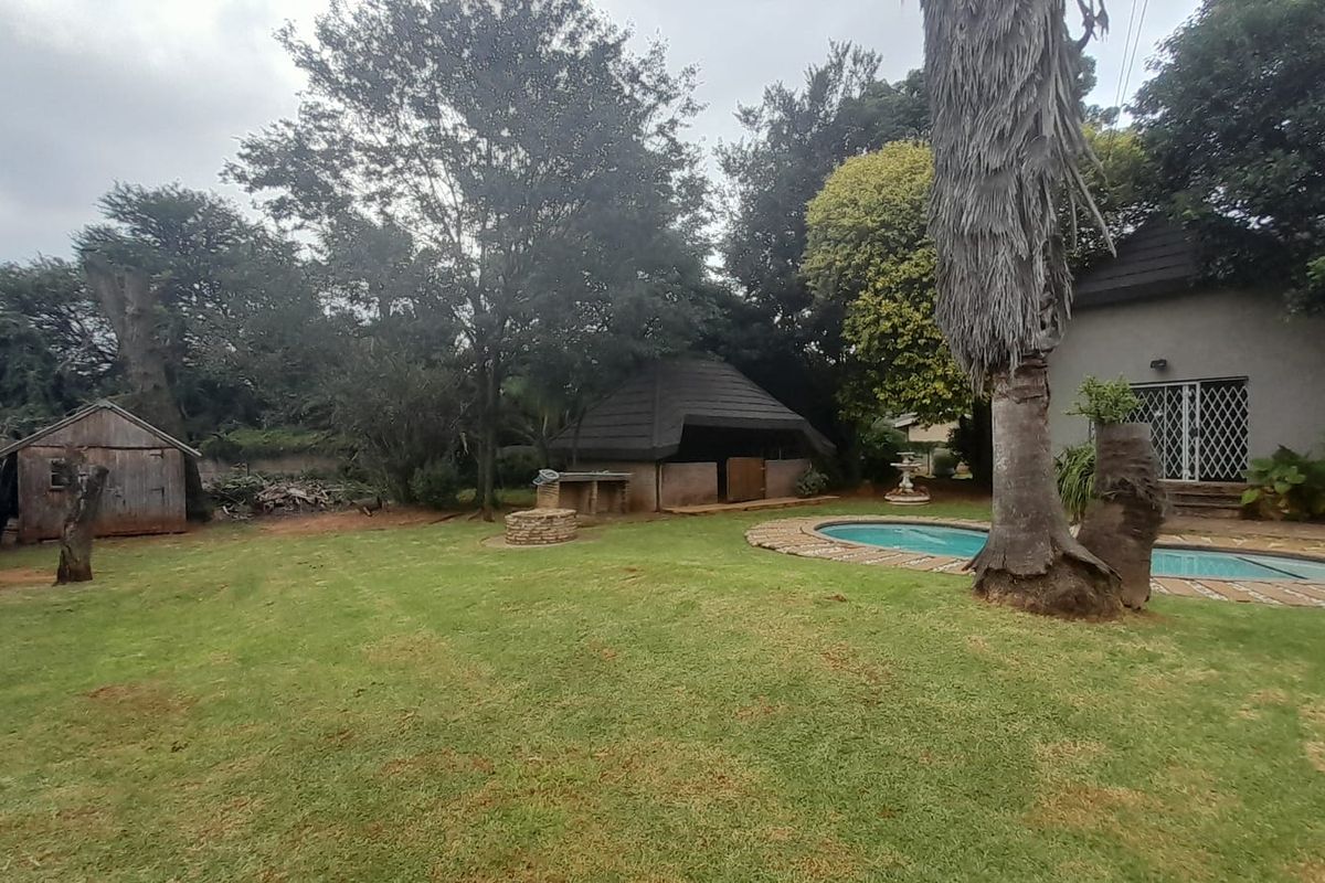 Spacious rear garden featuring a swimming pool, a thatched lapa entertainment area, and a detached wooden storage shed.