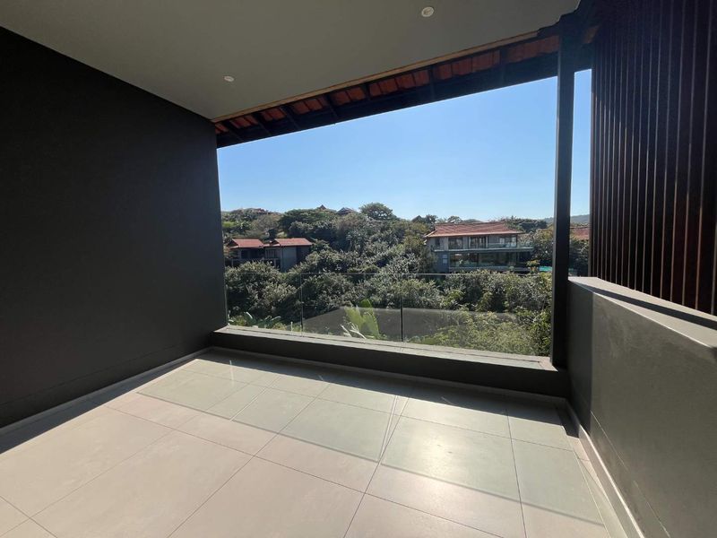 A modern covered balcony featuring tiled flooring, a sleek glass balustrade, and a timber slat screen, offering elevated views of the surrounding landscape.