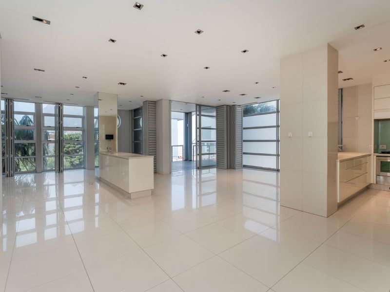 Spacious open-plan living and kitchen area featuring high-gloss tiled floors, modern built-in cabinetry, and large folding glass doors leading to an outdoor space.