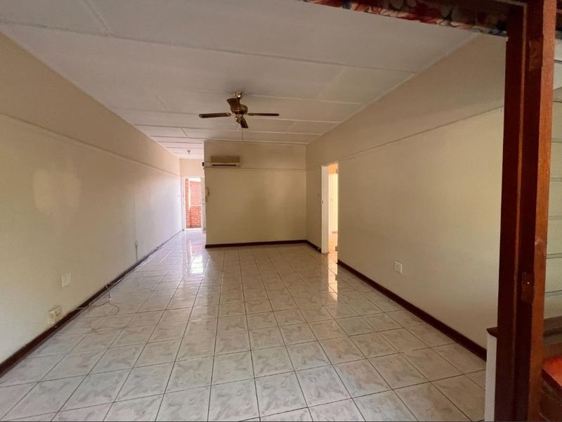 An empty, open-plan living area featuring tiled flooring, a ceiling fan, and a wall-mounted air conditioning unit.