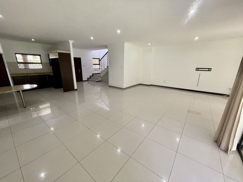 Spacious open-plan living area featuring polished porcelain floor tiles, recessed lighting, and a modern staircase, offering a bright and versatile layout.