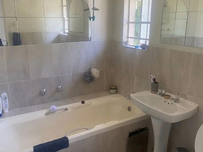 A dated bathroom featuring a bathtub with shower attachment, pedestal sink, toilet, and tiled finishes, requiring cosmetic updates to modernize the space.