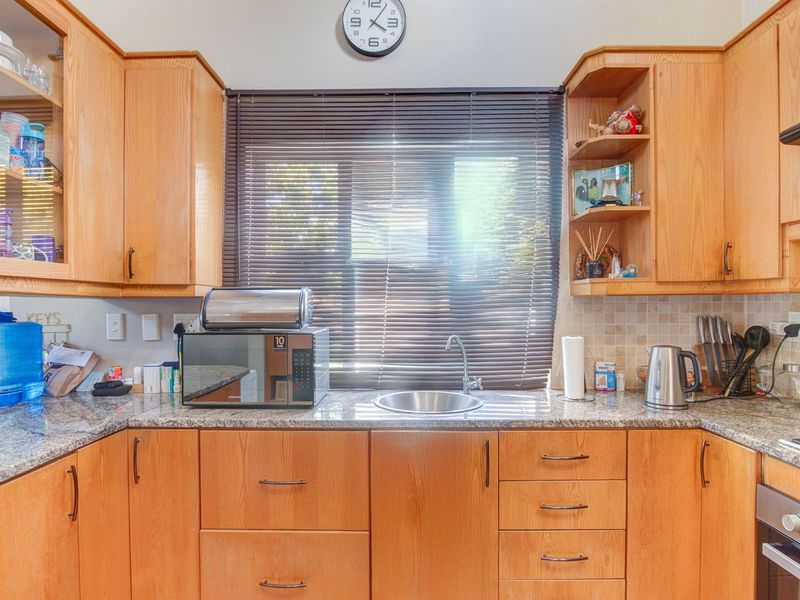 A functional kitchen featuring wooden cabinetry, granite countertops, a stainless steel sink, and a tiled backsplash with integrated oven.