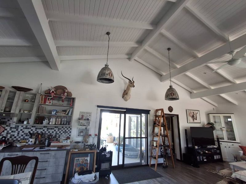 Spacious open-plan living area featuring high exposed beam ceilings, modern kitchen cabinetry with tiled backsplash, and large sliding doors leading to the patio.