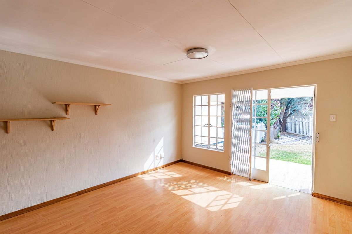 An empty living room featuring laminate flooring, security gate access to the garden, and natural light through timber-framed windows.