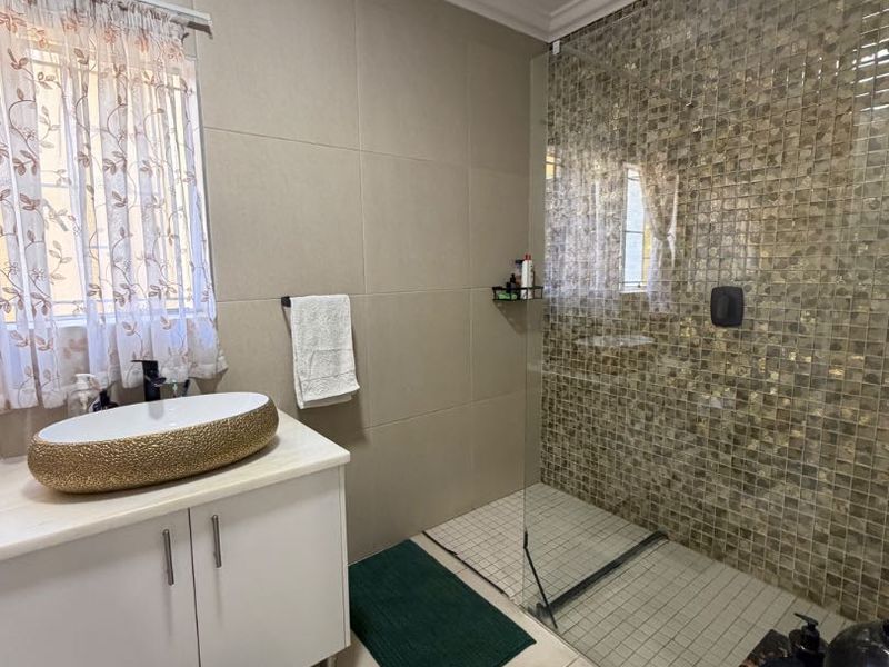Modern bathroom featuring a vessel sink on a vanity cabinet and a spacious walk-in shower with decorative mosaic tiling.
