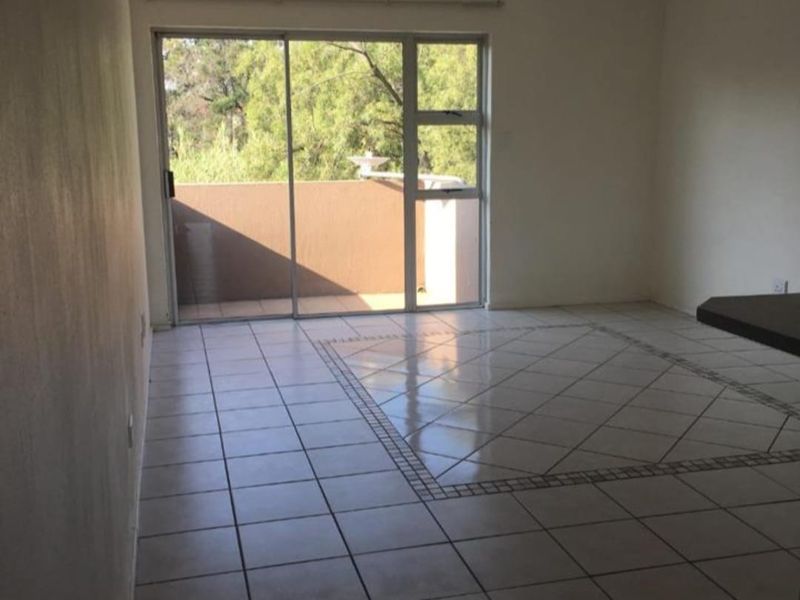 An empty living room featuring tiled flooring with a decorative inlay, a ceiling spotlight fixture, and a sliding glass door leading to a balcony.
