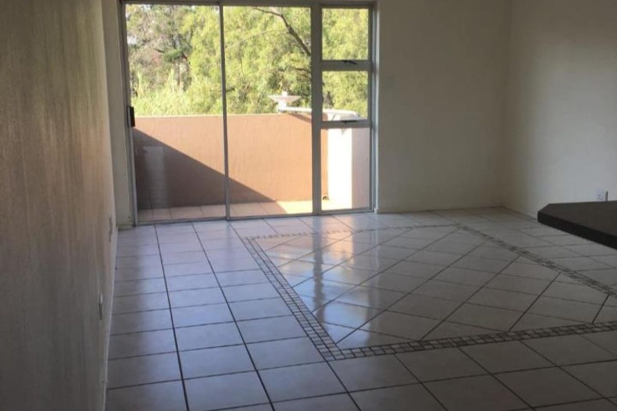 An empty living room featuring tiled flooring with a decorative inlay, a ceiling spotlight fixture, and a sliding glass door leading to a balcony.
