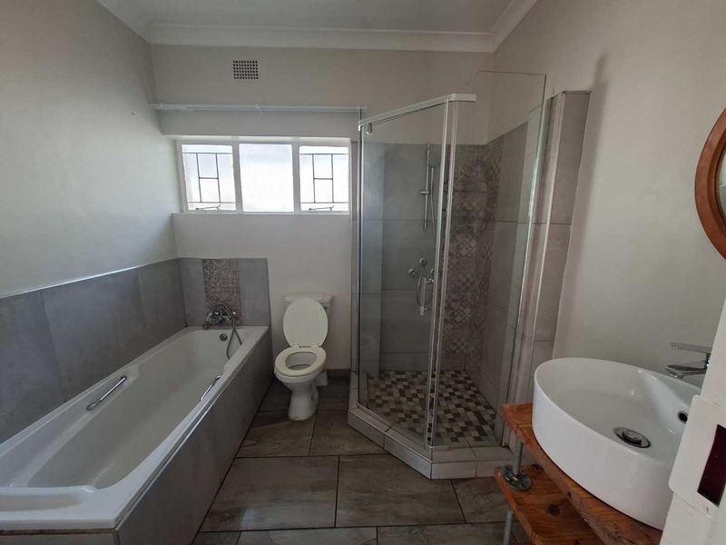 A clean, functional bathroom featuring a bathtub, separate shower enclosure, toilet, and a modern vessel sink on a wooden vanity base.