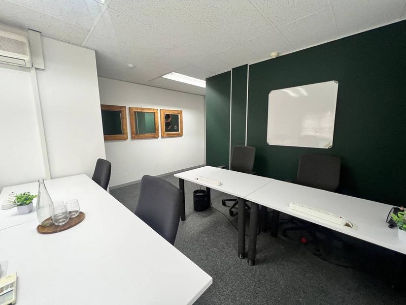 A functional office space featuring carpeted flooring, a suspended ceiling with recessed lighting, a wall-mounted air conditioning unit, and a dark accent wall.