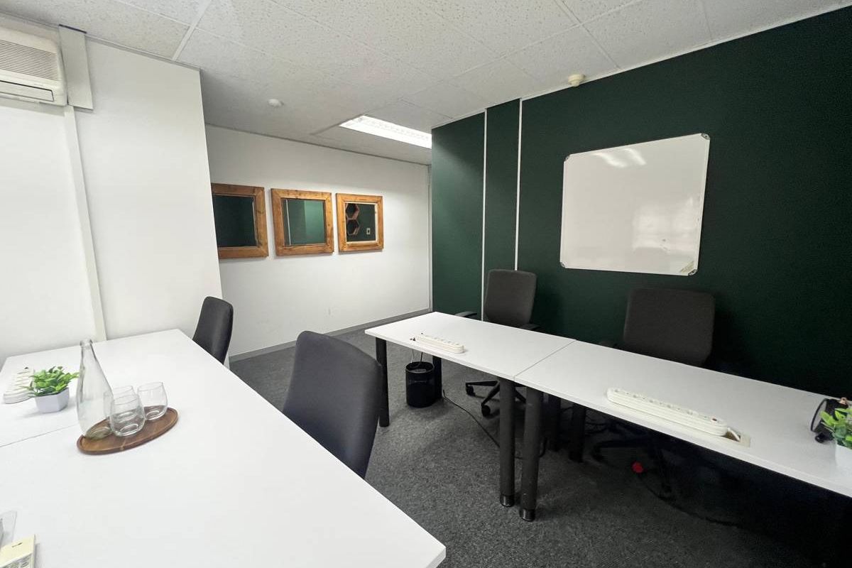 A functional office space featuring carpeted flooring, a suspended ceiling with recessed lighting, a wall-mounted air conditioning unit, and a dark accent wall.