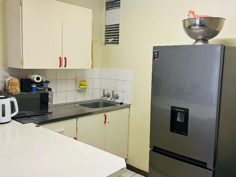 A compact kitchen featuring built-in cabinetry, a stainless steel sink, tiled backsplash, and tiled flooring, requiring some cosmetic updates to improve its overall condition.