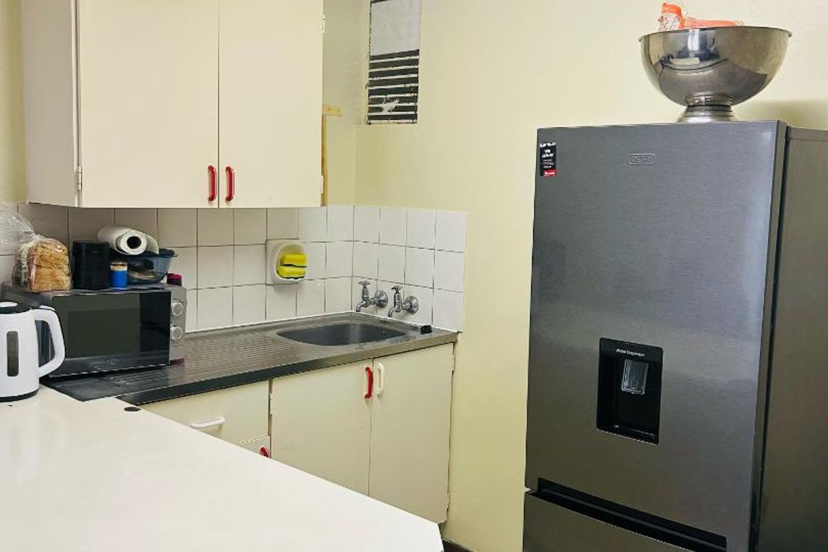 A compact kitchen featuring built-in cabinetry, a stainless steel sink, tiled backsplash, and tiled flooring, requiring some cosmetic updates to improve its overall condition.