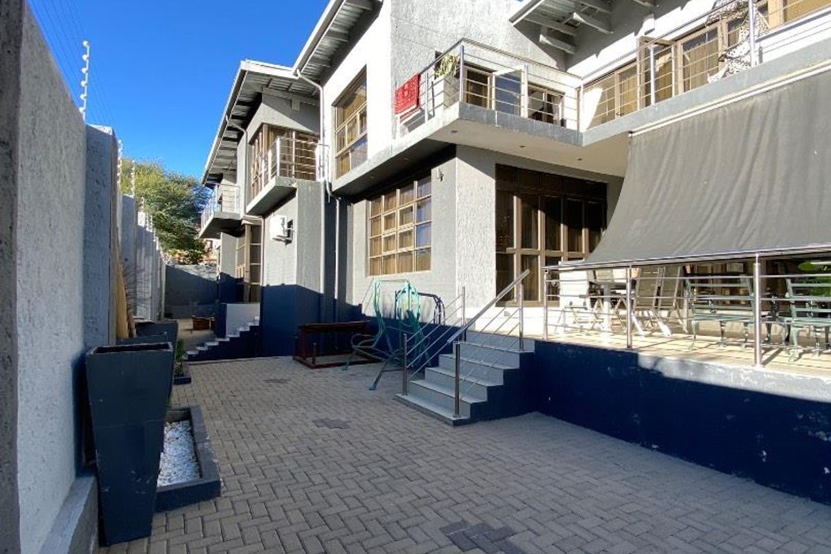 A view of the rear exterior of the house featuring paved courtyard, raised patio area with metal railings, and multi-level building facade.