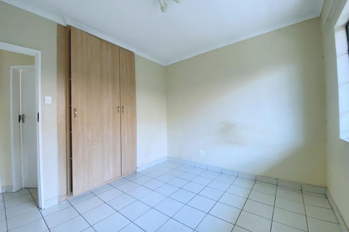 A vacant bedroom featuring light-colored floor tiles, built-in wooden cupboards, and neutral wall finishes.