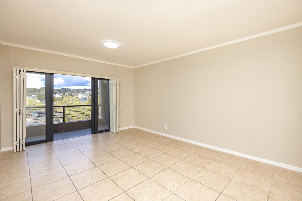 Spacious living area featuring neutral tiled flooring, crown molding, and large folding glass doors opening onto a private balcony with scenic views.