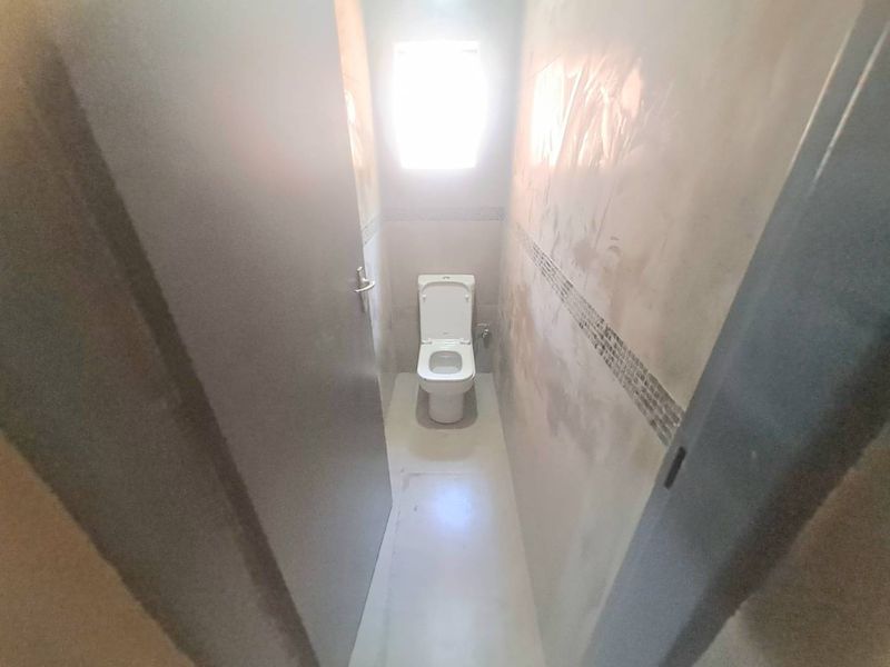 A small, unfinished bathroom featuring a toilet, tiled flooring, and wall tiling, currently requiring completion of wall plastering and finishing.