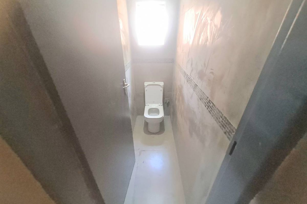 A small, unfinished bathroom featuring a toilet, tiled flooring, and wall tiling, currently requiring completion of wall plastering and finishing.