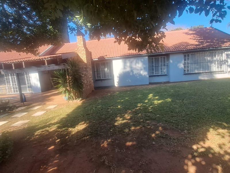 Rear view of a single-story house featuring a tiled roof, brick chimney, and a spacious garden area with paved walkway.