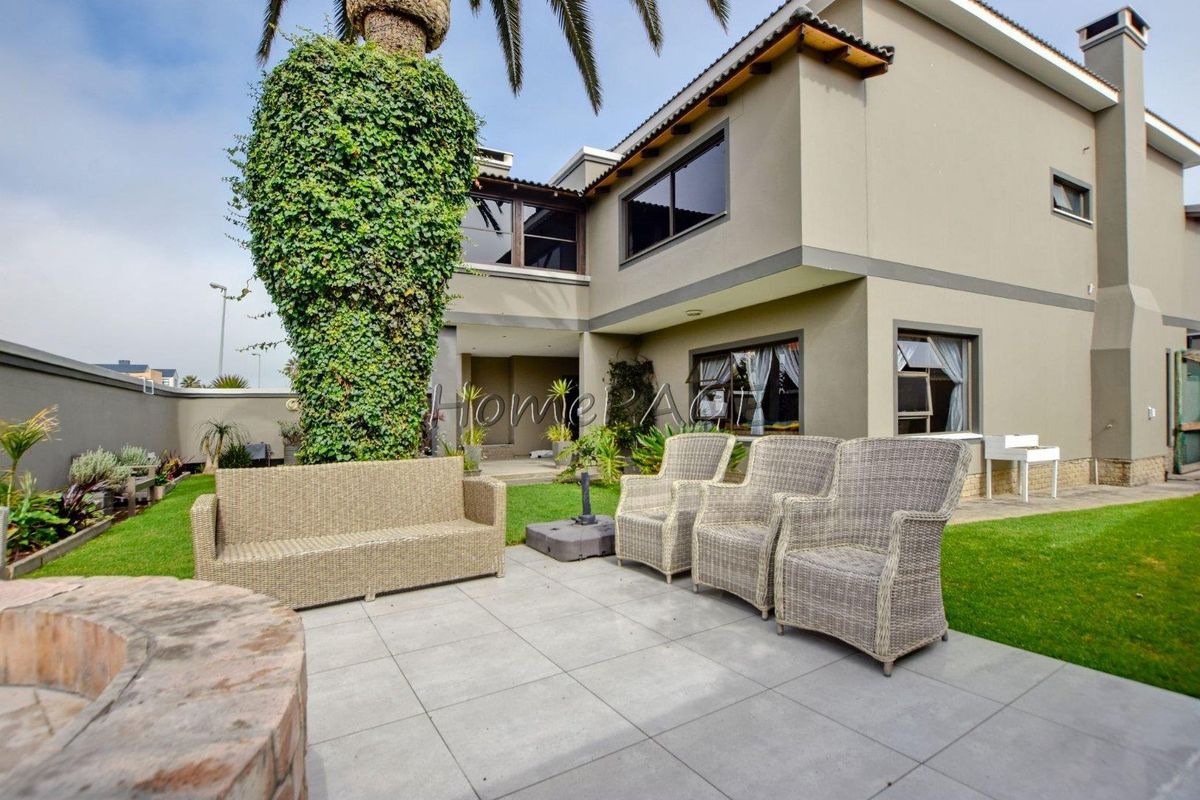Rear exterior view of the property featuring a paved patio area, a built-in brick fire pit, and a well-maintained garden with boundary walls.