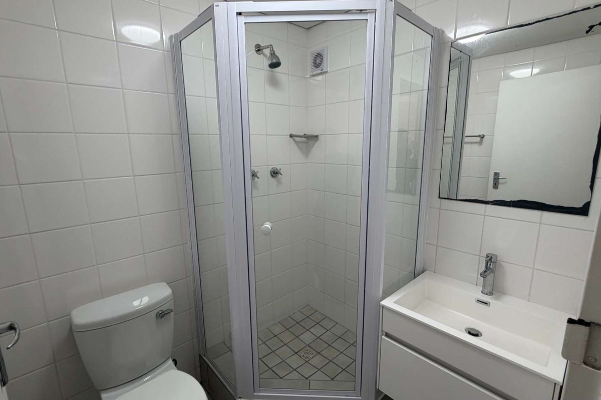 A functional bathroom featuring a corner shower enclosure, vanity basin with mixer tap, and white wall tiling.