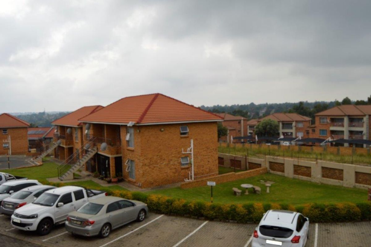 An elevated view of a townhouse complex featuring face-brick buildings with tiled roofs, communal lawn areas, and dedicated paved parking bays.