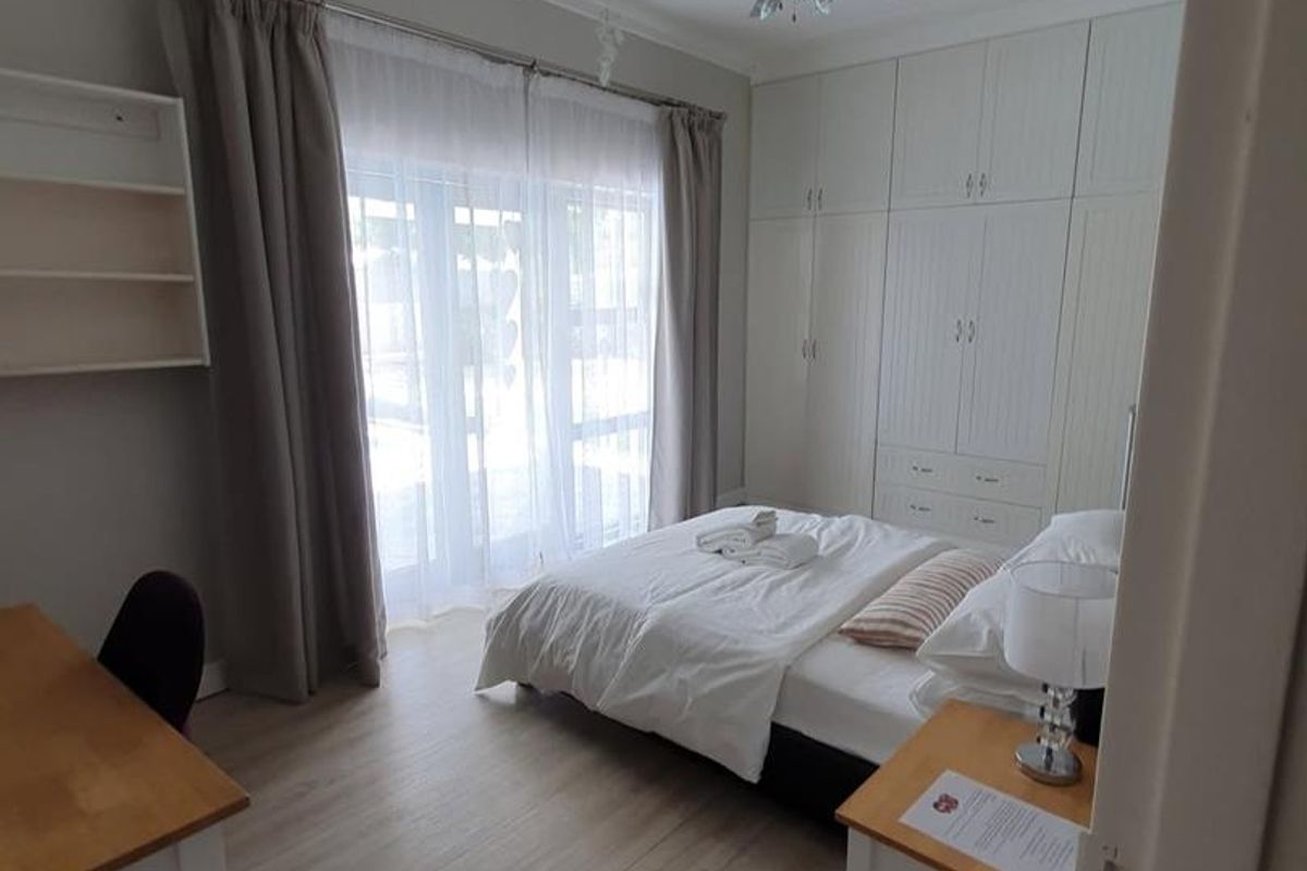 A well-maintained bedroom featuring built-in floor-to-ceiling cabinetry, light wood-look flooring, a ceiling fan, and sliding glass doors providing natural light.