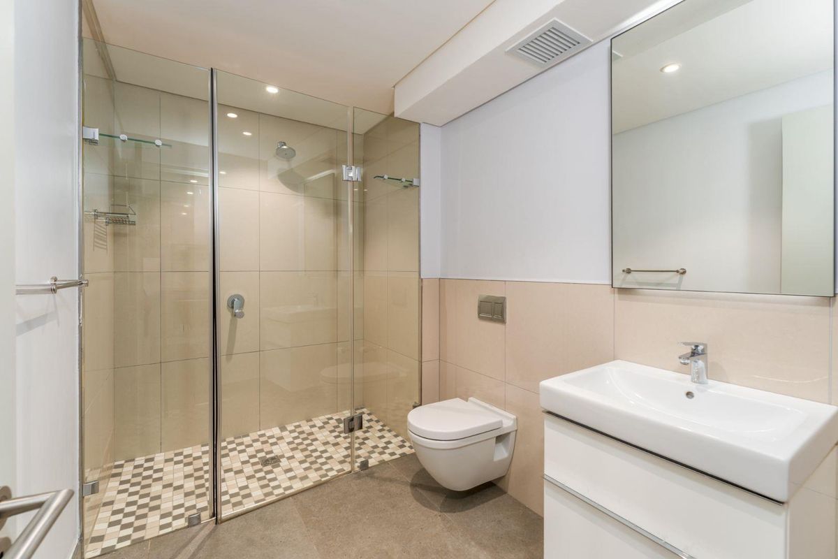 Modern bathroom featuring a frameless glass shower enclosure, wall-mounted toilet, and a sleek vanity with a basin and mirror.